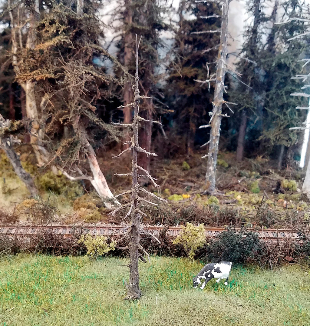 5 inch tall model snag tree presented on a HO scale railroad layout with HO scale cow named Daisy standing nearby for scale reference comparison and the railroad track in HO scale in the background.