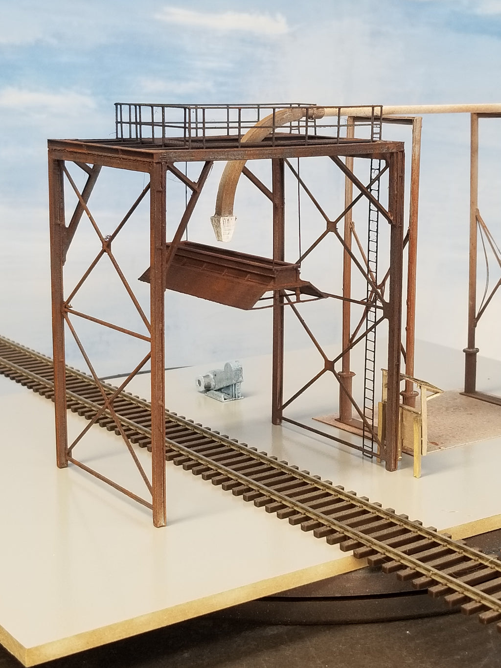 A built-up version of Coastman's Wood Chip Loader in HO scale, oblique end view, showing the feeder nozzle and tubing, chip bonnet, safety handrail, and main structural I-beam components, with HO scale track going underneath.