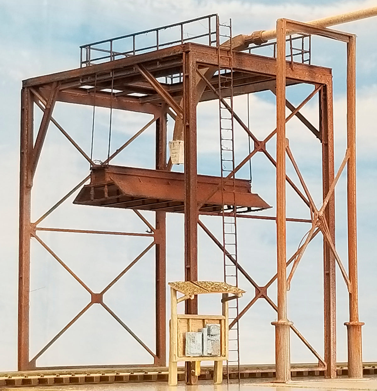 Ground view of the Coastman's HO scale Wood Chip Loader as built, showing the electrical panel detail, custom panel shack (not included), feeder support, feed tubing (not included), feeder nozzle, handrail, bonnet, and main I beam structural components, with HO scale track.