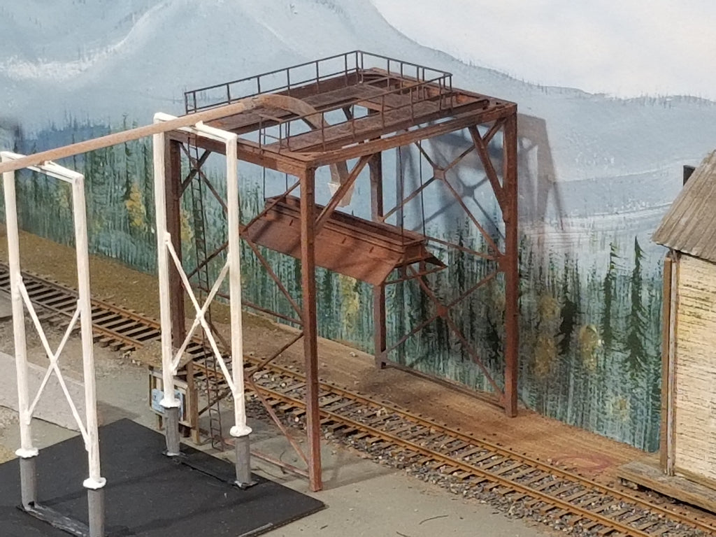 A built-up HO scale woodchip loader positioned over the tracks on Roger's HO scale Oregon Coast layout showing feeder support, feed tubing (not included), feeder nozzle, handrail, bonnet, and main I beam structural components, with HO scale track.