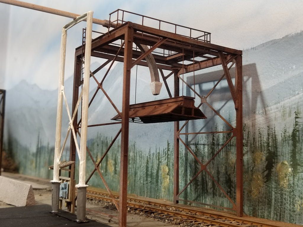 Ground level view of a built-up HO scale woodchip loader positioned over the tracks on Roger's HO scale Oregon Coast layout showing feeder support, feed tubing (not included), feeder nozzle, handrail, bonnet, and main I beam structural components, with HO scale track.