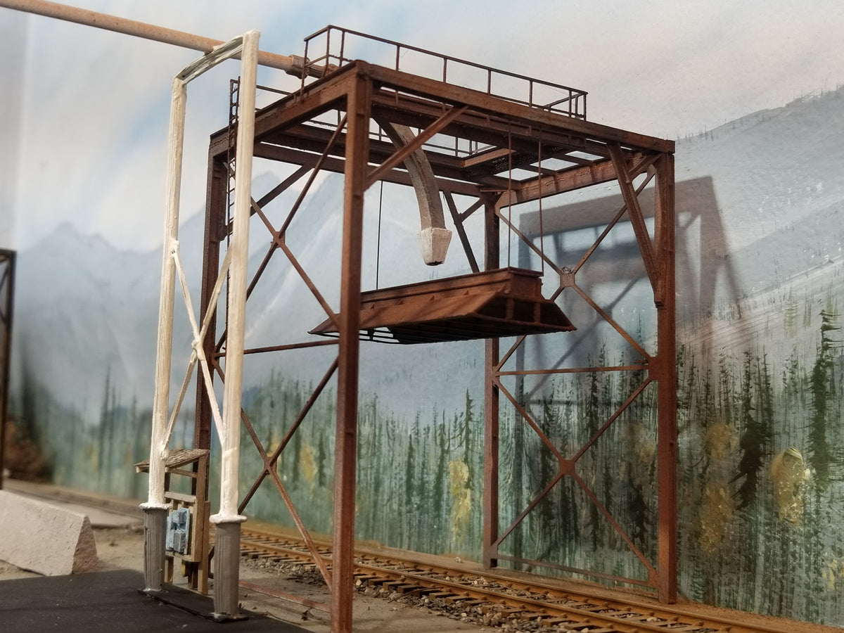 Ground level view of a built-up HO scale woodchip loader positioned over the tracks on Roger's HO scale Oregon Coast layout showing feeder support, feed tubing (not included), feeder nozzle, handrail, bonnet, and main I beam structural components, with HO scale track.