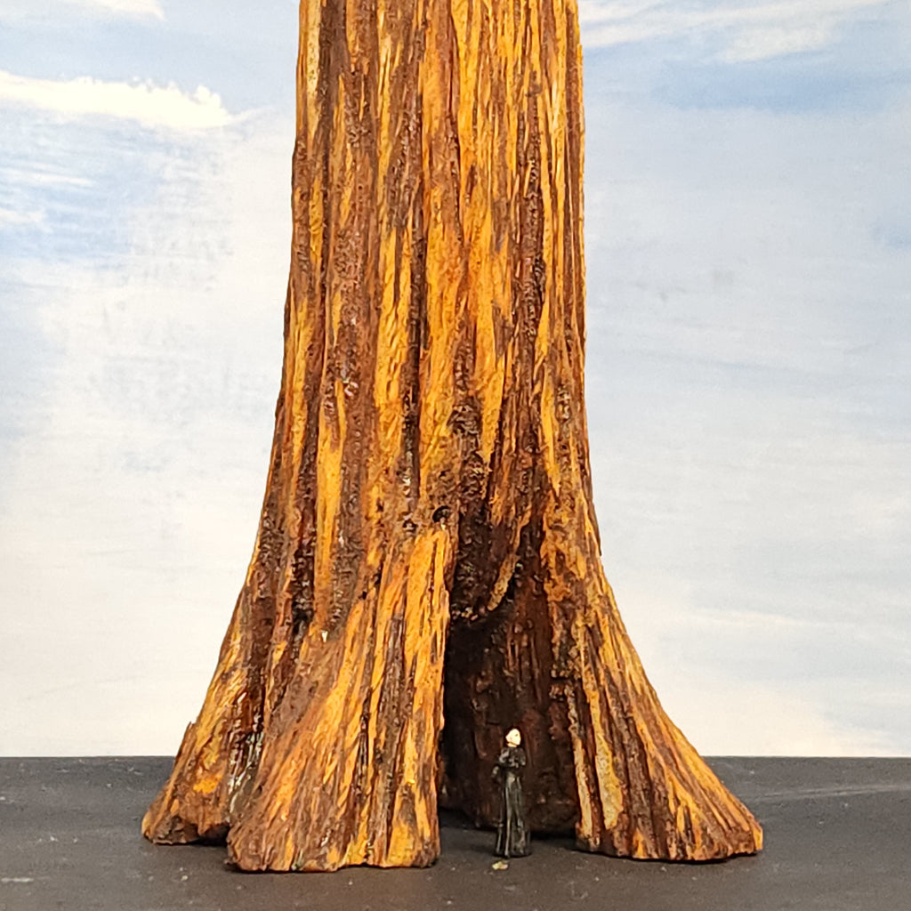 Large redwood wooden sculpture resembling a redwood tree with a person standing inside an old cavity, against a cloudy sky.