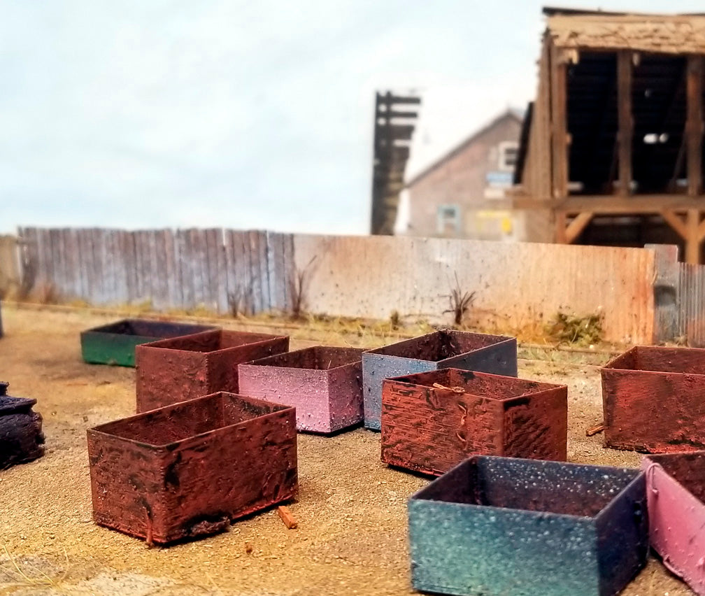 Rust-colored scrap metal bins presented upon a HO scale 1:87 diorama with a wooden structure and fence in the background. Made in USA by Coastmans Scenic Products CSP LLC