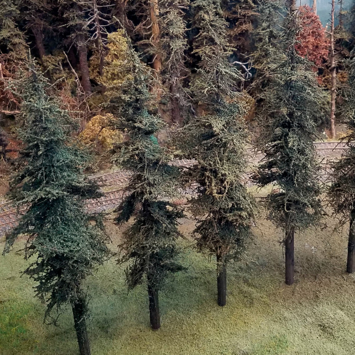 Four Coastman's Standard model fir trees displayed on a model railroad layout photo from above oblique angle to show exclusive green foliage material with model railroad scenery in the background.