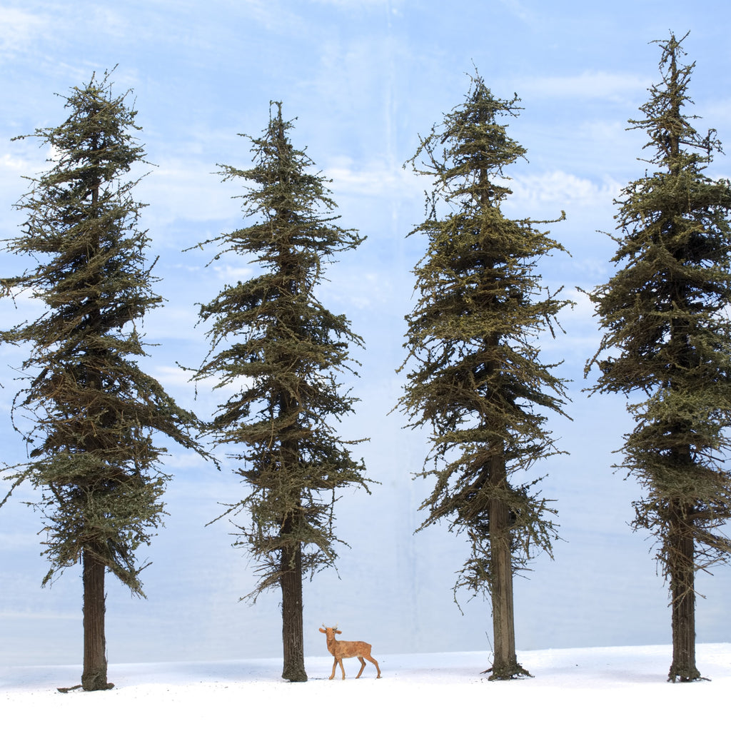 Four Coastman's 9-inches tall Standard model fir trees with HO scale deer for reference on a white foam base that looks like snow.