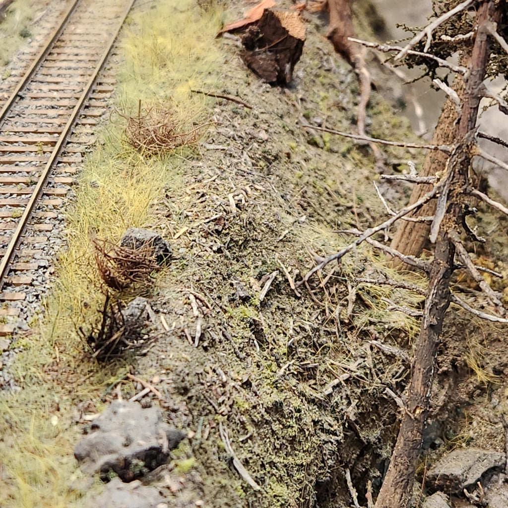 Bits of Coastman's Forest Floor material as seen on Roger's Port of Tillamook Bay model railroad layout in HO scale also including an HO scale snag tree near a creek and railroad tracks.