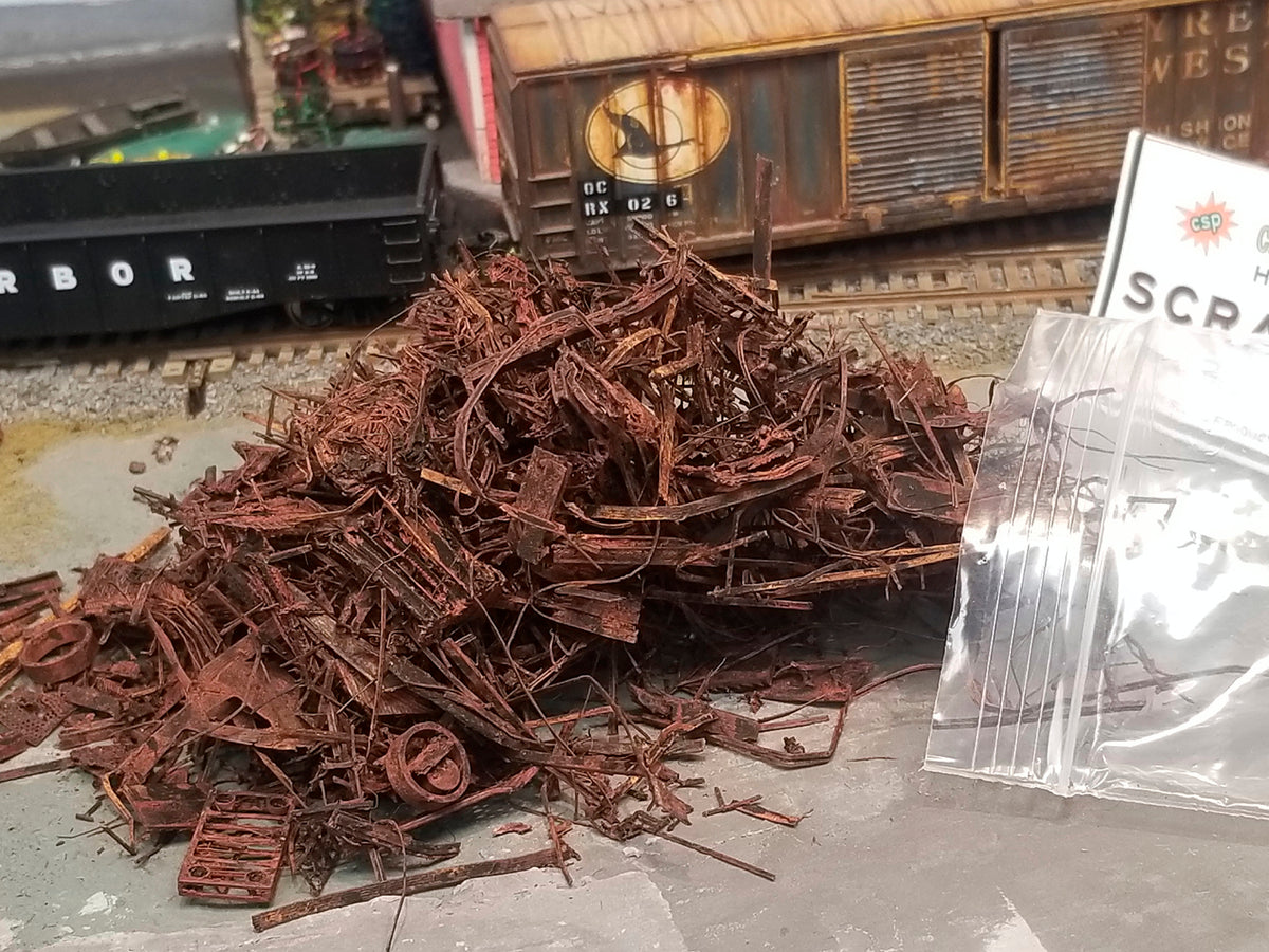 Close up shot of Coastman's HO scale SCRAP METAL, photo taken on Roger's OCRX HO scale model railroad layout, showing contents including metal rims, grating, matresses, and shredded metal which is actually made of PLA, with HO scale railroad cars in the background.